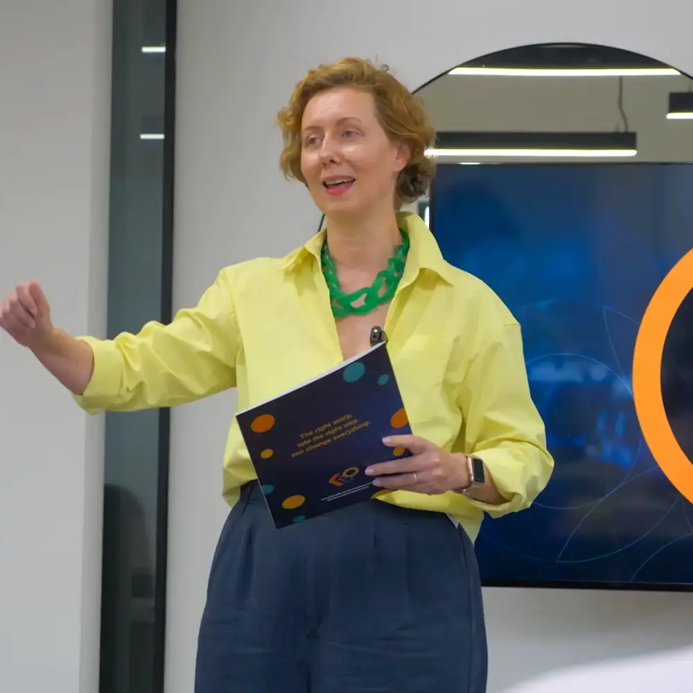 Woman in a yellow shirt presenting while holding a Kindler booklet
