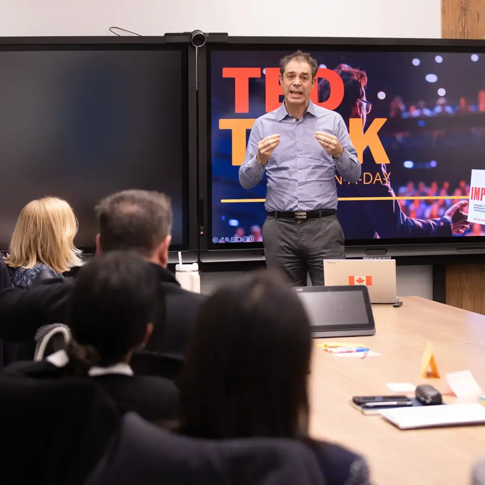 Facilitator presenting to a small group in front of a TED Talk in a Day screen