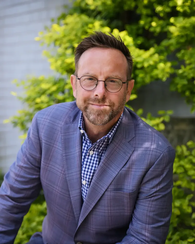Headshot of Nick Kindler, wearing glasses and a blazer.