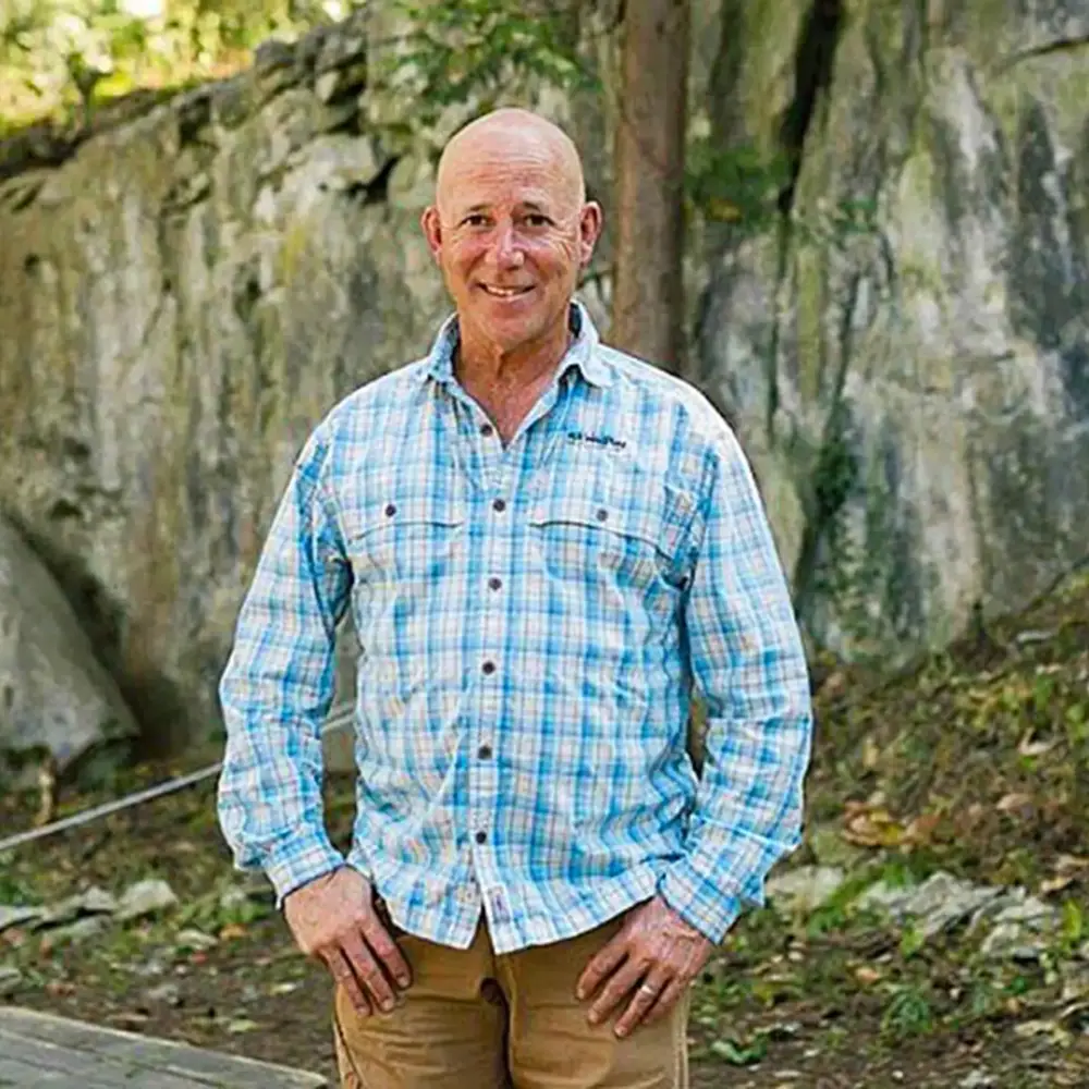Tom Benson headshot, standing in front of a rock face in a plaid shirt
